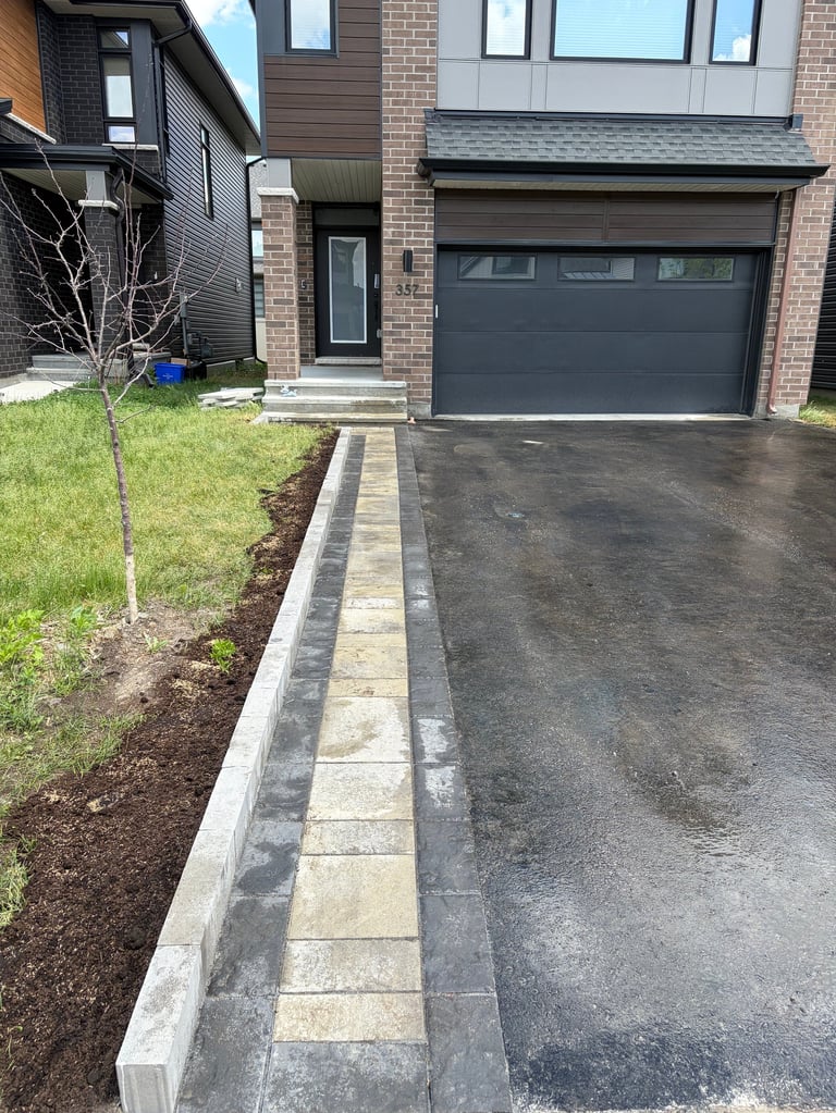 Modern brick house with dark garage door, concrete driveway with decorative border edging, and landscaping with young tree