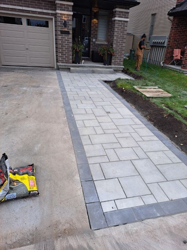 New paver walkway being installed in front of brick house with garage, extending to front entrance