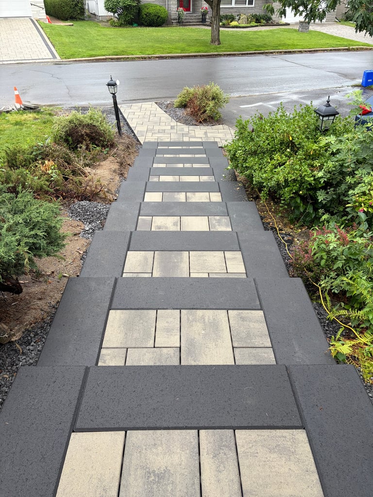 Aerial view of residential pathway with gray asphalt borders and light stone pavers in center, flanked by green landscaping and shrubs
