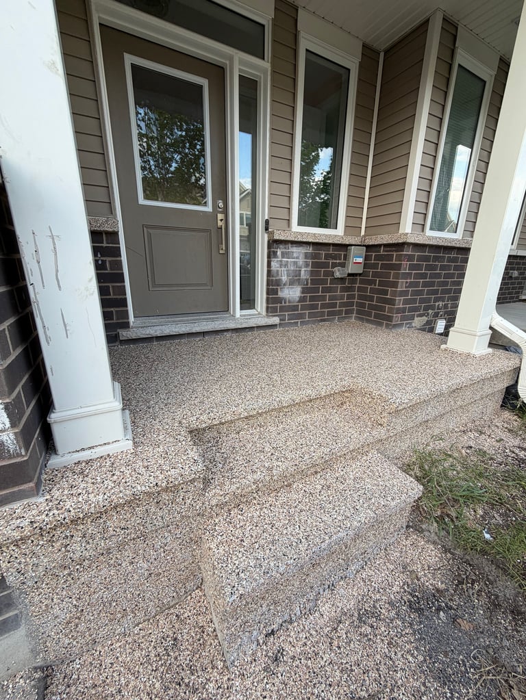 Front porch entrance with gray door, transom windows, brick siding, and decorative gravel flooring.