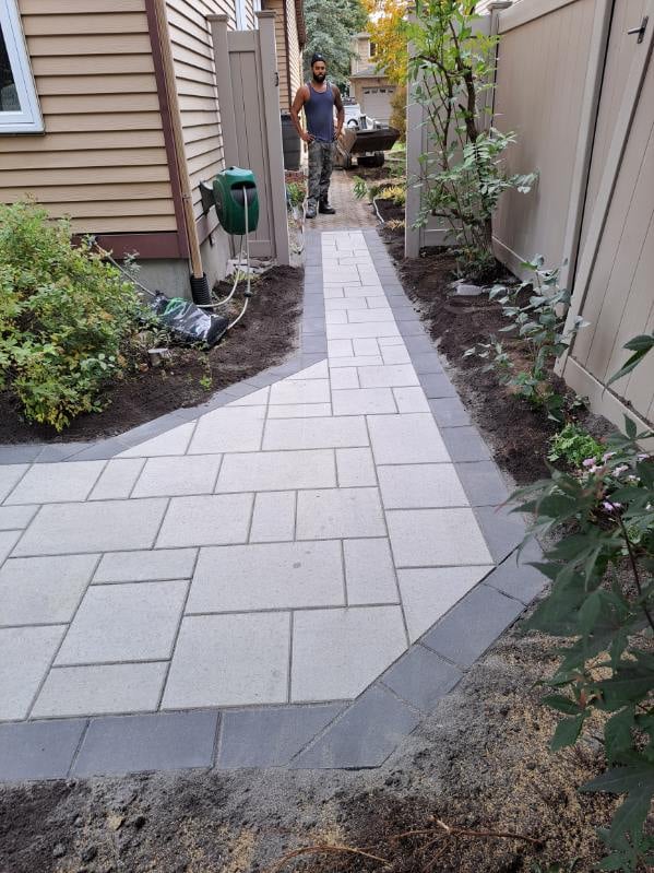 Narrow paved pathway between residential buildings with landscaping and a person walking in the distance