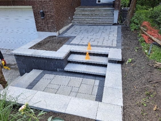 Modern patio with geometric paving stones, brick wall backdrop, and metal fire pit feature with decorative planters