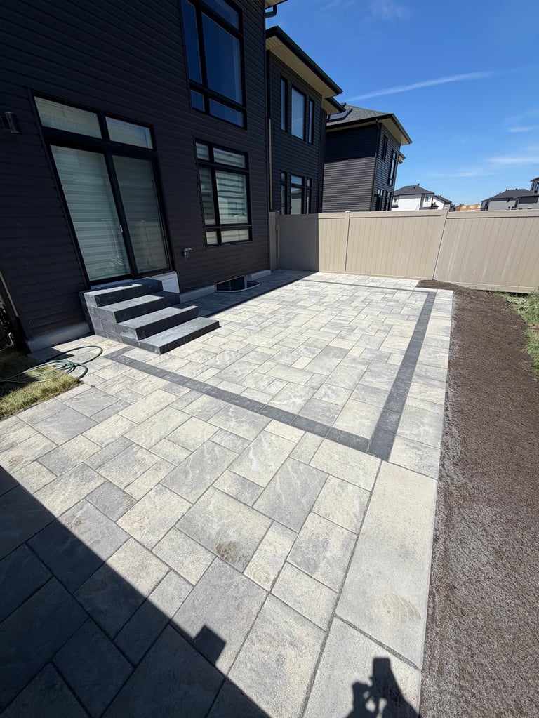 Modern black house with patio featuring decorative stone pavers and white metal fence on sunny day