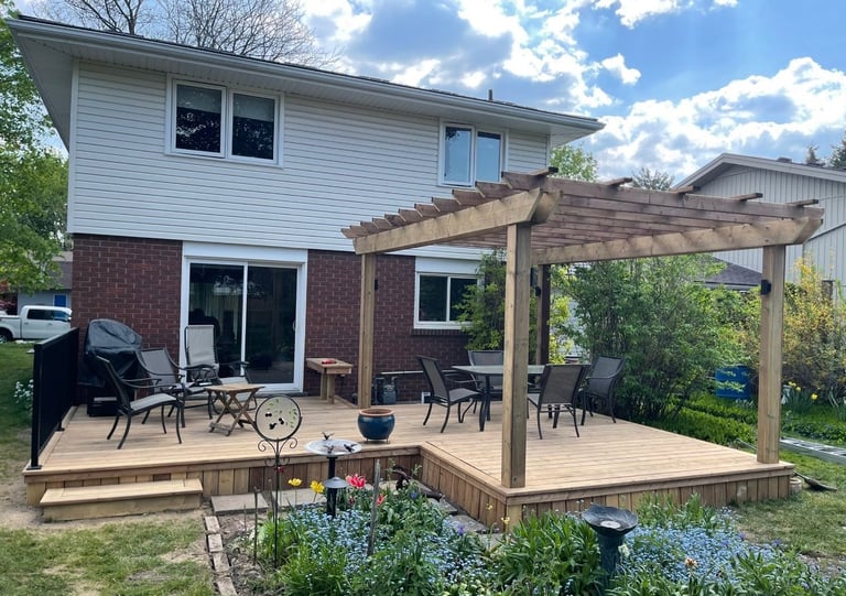 Backyard deck with pergola attached to brick and siding home, featuring patio furniture and surrounded by landscaping