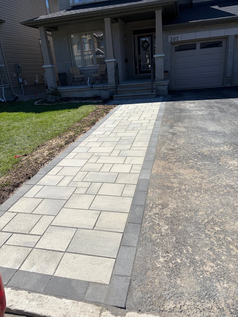 New paver walkway leading to a modern home entrance with a garage, lawn, and landscaping