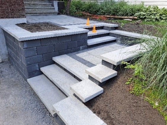 Modern landscaping with concrete steps leading to a raised garden bed with black block walls and two orange torches