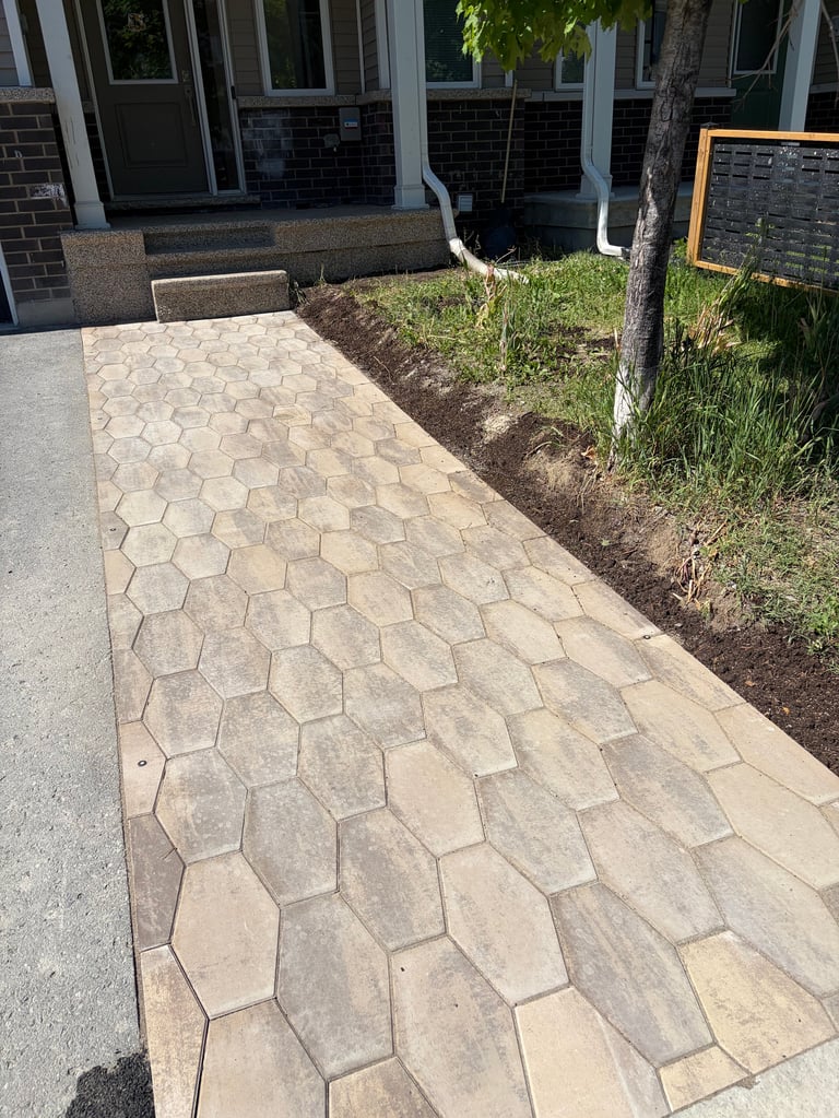 Paver stone walkway leading to a modern home entrance with landscaping and a chalkboard sign on the right